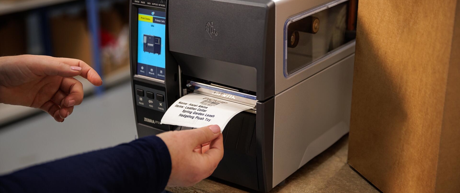 Der Etikettendrucker Zebra ZT231 druckt ein Versandetikett, eine Hand greift nach dem Etikett.